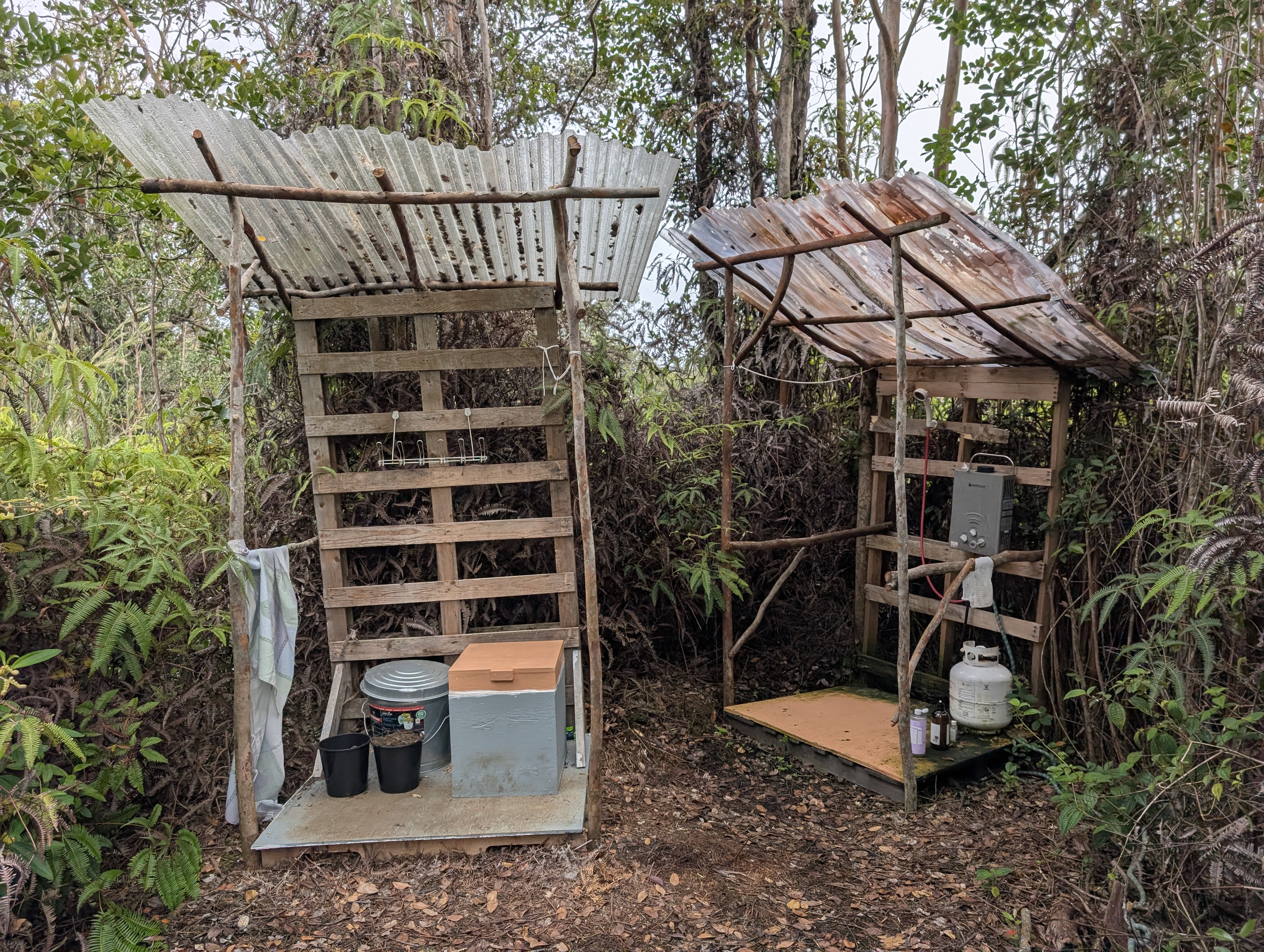 Composting toilet stall and jungle shower under corrugated roofs